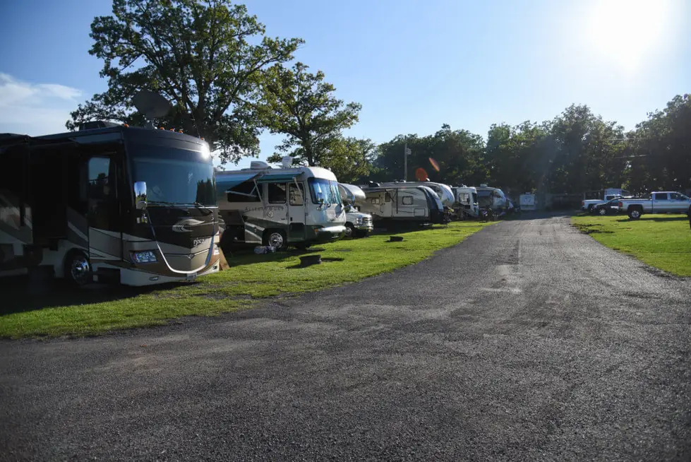 Gravel lane between motorhomes and fifth wheels on mown grass, big oak trees and blue sky